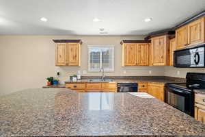 Kitchen with black appliances, a textured ceiling, light brown cabinetry, recessed lighting, and dark stone counters