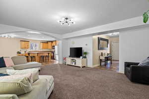 Carpeted living room featuring a chandelier, arched walkways, and a textured ceiling