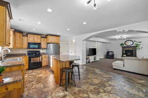 Kitchen with arched walkways, a kitchen breakfast bar, black appliances, a kitchen island, and recessed lighting