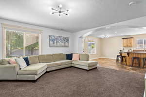 Living room featuring a chandelier, arched walkways, a textured ceiling, and dark carpet