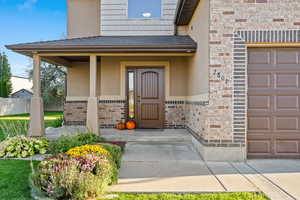 Doorway to property with roof with shingles, covered porch, a garage, and stucco siding