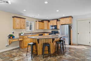 Kitchen featuring black appliances, a kitchen breakfast bar, a center island, recessed lighting, and dark stone finish flooring