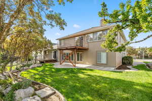 Rear view of house featuring a patio, a lawn, stucco siding, a chimney, and a wooden deck