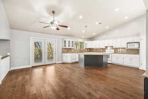 Kitchen with backsplash, white cabinetry, a kitchen island, dark wood-type flooring, and white appliances