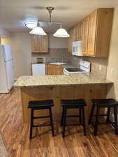 Mother-in-law Kitchen featuring a kitchen breakfast bar, white appliances, backsplash, a peninsula, and a textured ceiling