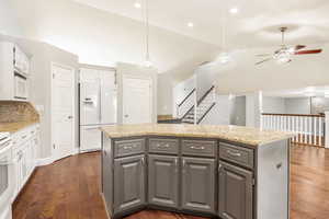 Kitchen featuring a kitchen island, white appliances, decorative light fixtures, ceiling fan, and light stone counters