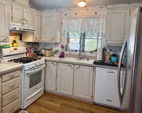 Kitchen with white appliances, under cabinet range hood, light countertops, dark wood-style flooring, and light brown cabinetry