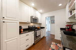 Kitchen with appliances with stainless steel finishes, dark wood-style floors, dark stone countertops, white cabinets, and recessed lighting