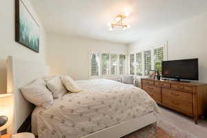 Carpeted bedroom featuring multiple windows, a chandelier, and a textured ceiling