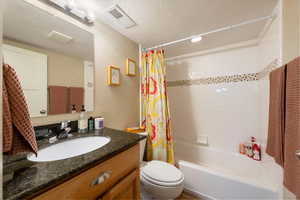 Full bath featuring shower / bath combo with shower curtain, a textured wall, a textured ceiling, and vanity