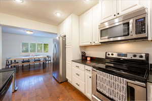Kitchen featuring stainless steel appliances, dark wood-style flooring, white cabinetry, dark stone counters, and a textured ceiling
