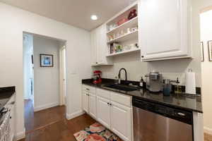 Kitchen featuring open shelves, stainless steel dishwasher, white cabinetry, dark wood finished floors, and dark stone counters