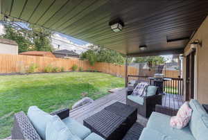 Fenced backyard with a wooden deck, an outdoor living space, a grill, and a trampoline