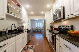 Kitchen with stainless steel appliances, dark stone counters, open shelves, white cabinetry, and recessed lighting