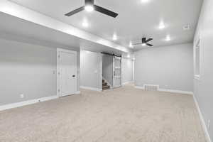 Finished basement featuring a barn door, a ceiling fan, light colored carpet, and stairway
