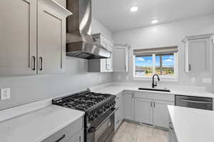 Kitchen with high end black range oven, wall chimney range hood, stainless steel dishwasher, light wood-style floors, and light stone countertops