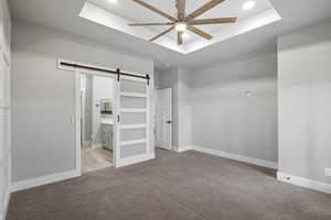 Unfurnished bedroom featuring a raised ceiling, a barn door, light colored carpet, ensuite bathroom, and recessed lighting