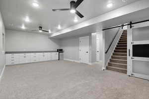 Finished below grade area with a barn door, light carpet, a ceiling fan, stairs, and freestanding refrigerator
