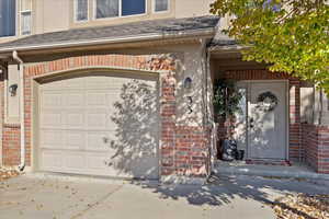 Property entrance featuring a shingled roof, brick siding, a garage, and stucco siding