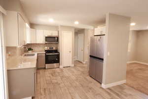Kitchen with stainless steel appliances, light stone countertops, tasteful backsplash, white cabinetry, and light wood-style flooring