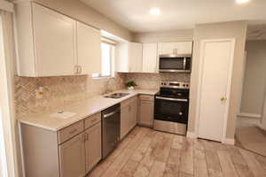 Kitchen featuring tasteful backsplash, appliances with stainless steel finishes, light stone countertops, light wood-style floors, and recessed lighting
