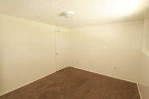 Unfurnished room featuring a textured ceiling and dark colored carpet