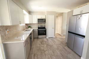 Kitchen with stainless steel appliances, tasteful backsplash, light stone counters, light wood-style floors, and white cabinets