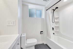 Bathroom featuring shower / tub combo with curtain, dark tile patterned flooring, and vanity