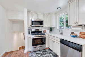 Kitchen featuring stainless steel appliances, light wood-style floors, white cabinets, and light stone countertops