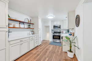 Kitchen with white cabinets, open shelves, light countertops, and stainless steel appliances