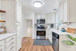 Kitchen featuring stainless steel appliances, white cabinets, open shelves, and light wood-style flooring