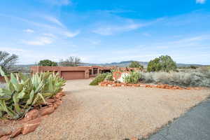 View of front of property with a mountain view, gravel driveway, stucco siding, and an attached garage