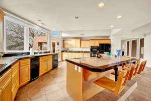 Kitchen featuring tile countertops, a center island with sink, a kitchen bar, black appliances, and recessed lighting