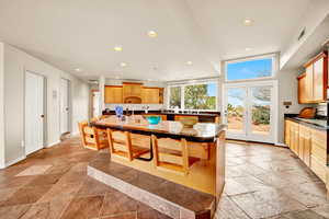 Kitchen with recessed lighting, a kitchen bar, stone tile floors, a kitchen island with sink, and tile counters