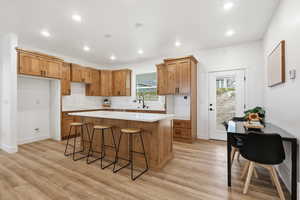 Kitchen featuring brown cabinets, recessed lighting, a center island, a kitchen breakfast bar, and light wood finished floors