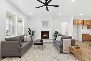 Living area featuring light wood-style floors, recessed lighting, a large fireplace, a ceiling fan, and arched walkways