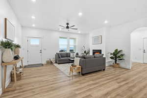 Living room featuring a ceiling fan, light wood-style floors, recessed lighting, arched walkways, and a fireplace