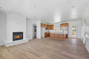 Kitchen featuring arched walkways, open floor plan, a large fireplace, brown cabinetry, and recessed lighting