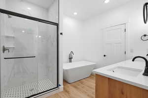 Full bathroom featuring double vanity, light wood-style floors, a marble finish shower, a freestanding bath, and recessed lighting