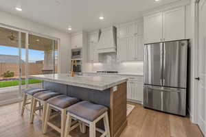 Kitchen with appliances with stainless steel finishes, light wood-style floors, backsplash, custom exhaust hood, and recessed lighting