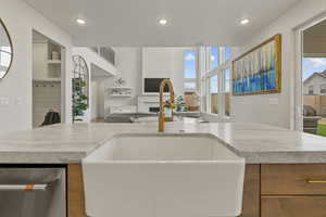 Kitchen featuring brown cabinets, dishwasher, open floor plan, recessed lighting, and a fireplace