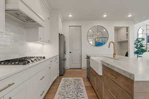 Kitchen with white cabinets, light wood finished floors, premium range hood, light stone counters, and recessed lighting