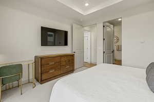 Bedroom featuring light colored carpet, recessed lighting, a raised ceiling, and ensuite bath