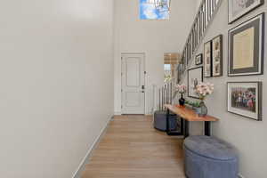 Hall with light wood-style flooring, a towering ceiling, and stairs