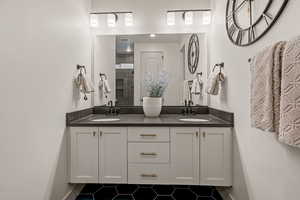 Full bathroom featuring double vanity, a tile shower, and dark tile patterned flooring