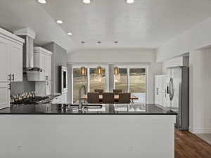 Kitchen featuring hanging light fixtures, stainless steel fridge with ice dispenser, a peninsula, white cabinets, and vaulted ceiling