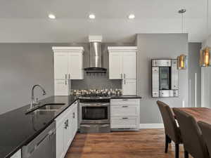 Kitchen with stainless steel appliances, dark stone counters, pendant lighting, wall chimney exhaust hood, and white cabinetry