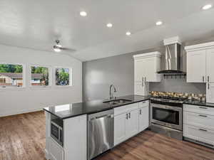 Kitchen with a peninsula, stainless steel appliances, white cabinetry, recessed lighting, and wall chimney exhaust hood