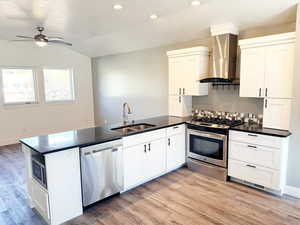 Kitchen featuring a peninsula, appliances with stainless steel finishes, wall chimney range hood, light wood-style flooring, and backsplash