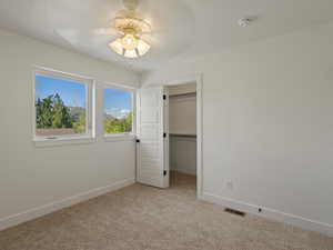 Unfurnished bedroom featuring a walk in closet, light colored carpet, and a ceiling fan